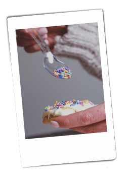 Instax picture of a hand pouring sprinkles on iced cookies