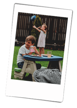 Instax picture of a girl playing with a ball and a boy sitting at a kids' picnic table