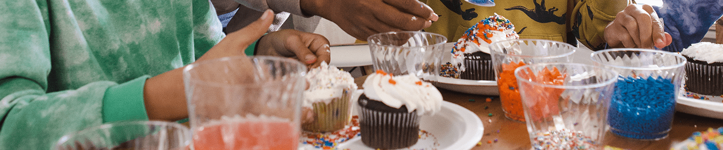 Hands pouring sprinkles on cupcakes