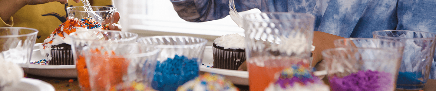 Hands pouring sprinkles on cupcakes