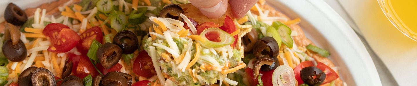 Hand dipping tortilla chip into 7 layer dip