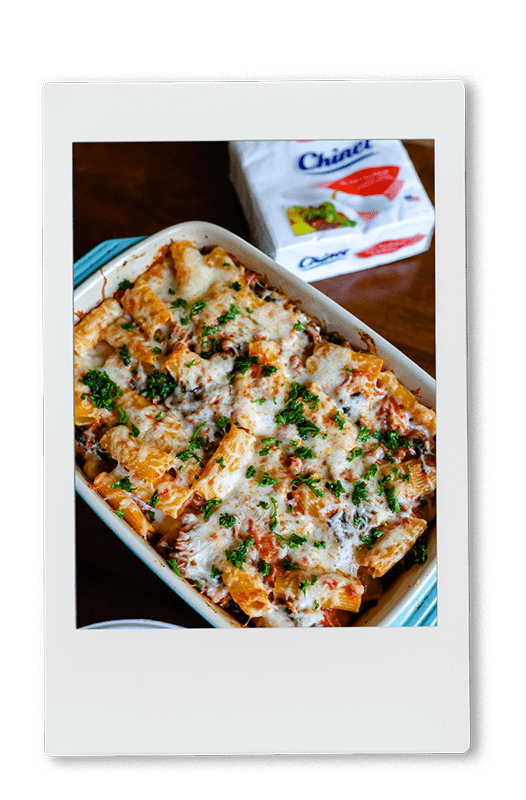Instax of a cheesy pasta bake in a baking dish next to Chinet Classic napkins
