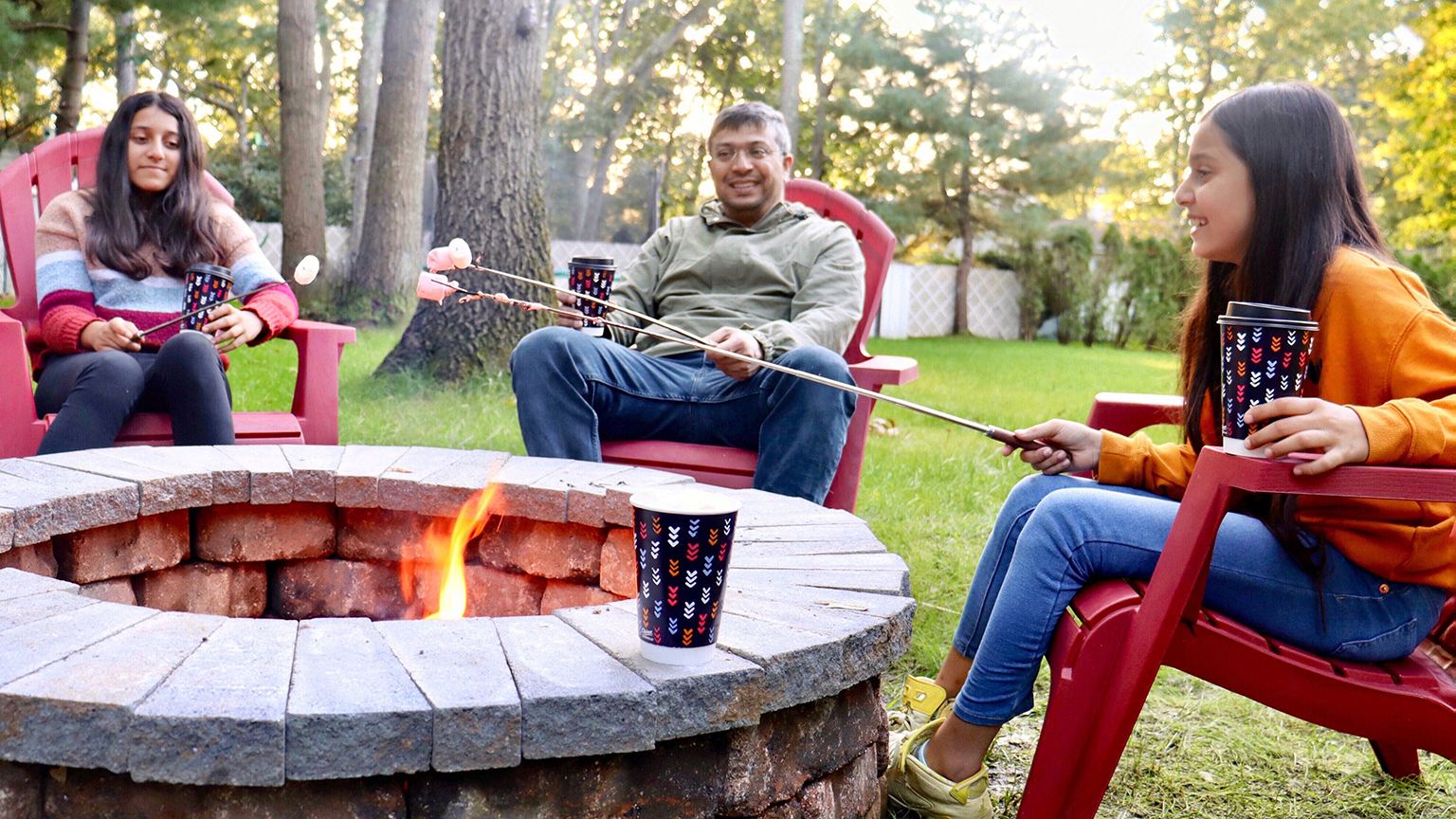 Family sitting around a bonfire roasting marshmallows and drinking hot chocolate from a Chinet Comfort cup