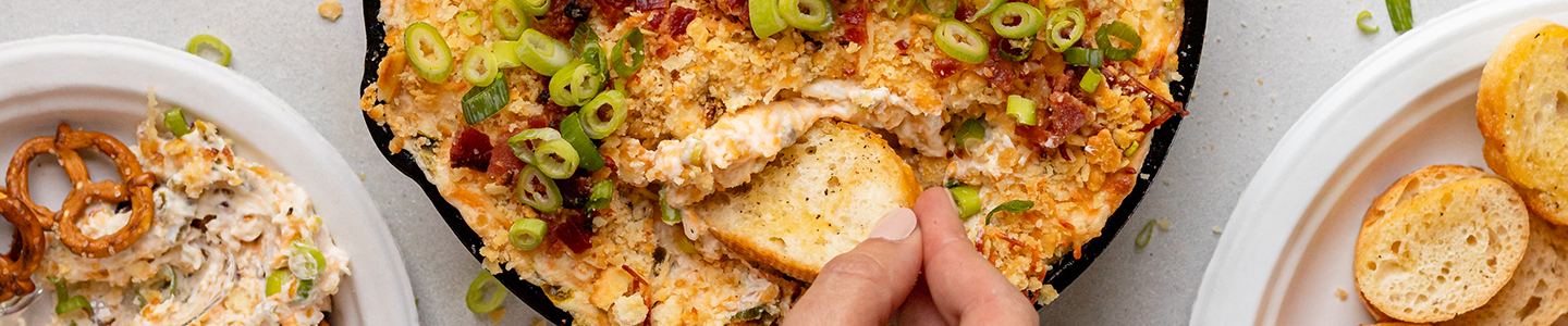 Hand scooping jalapeno popper dip from a cast iron pan with a tortilla chip