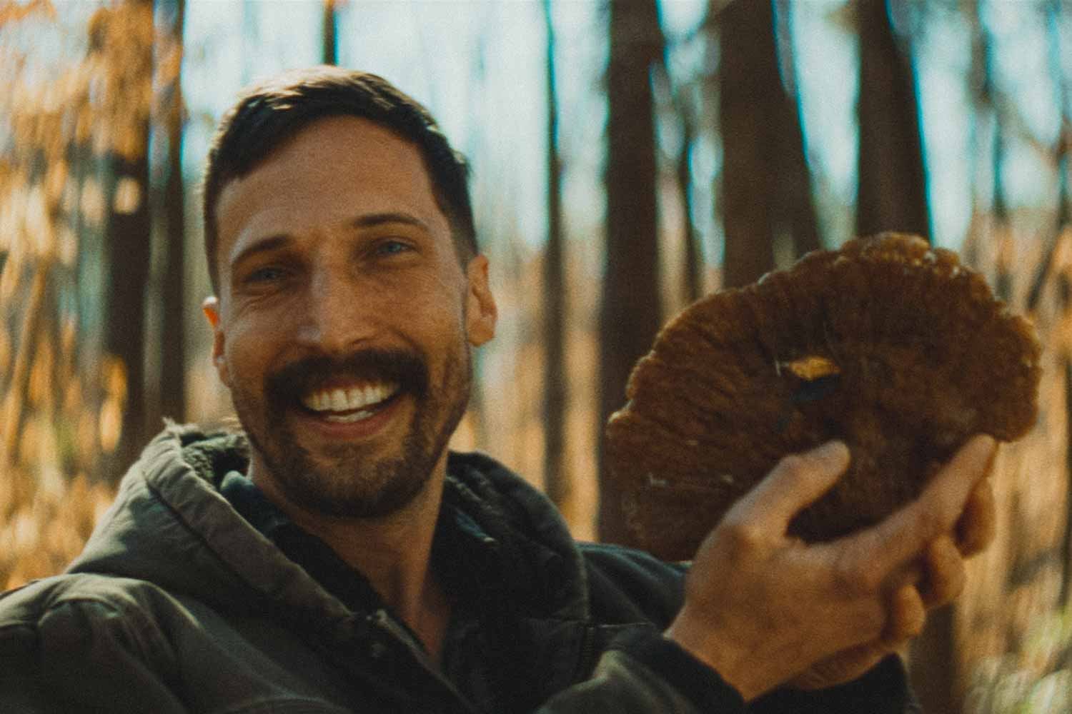 A smiling man holding up a freshly harvested mushroom