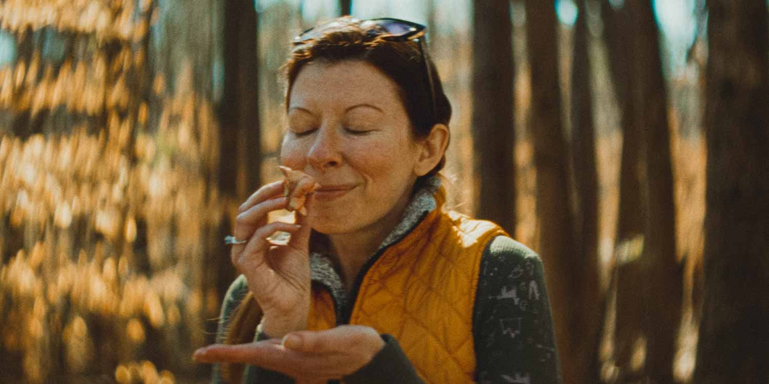 A woman in a yellow vest happily smelling a freshly harvested mushroom