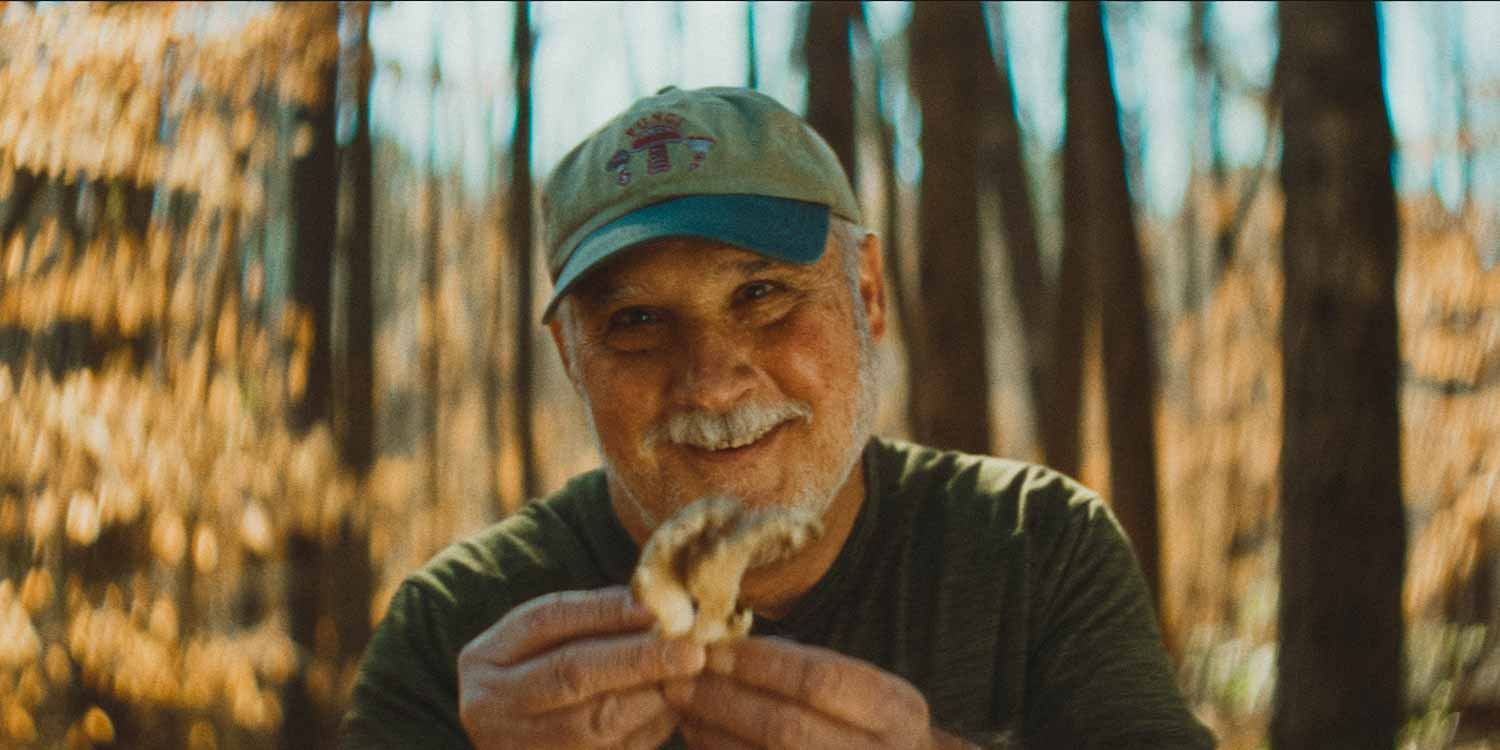 Man in cap smiling and showing off the mushroom he found