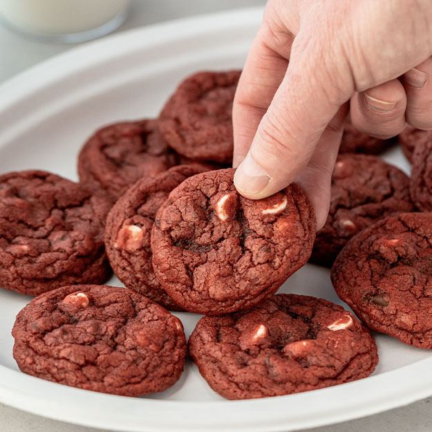 Hand picking up a red velvet cookie from Chinet Classic plate