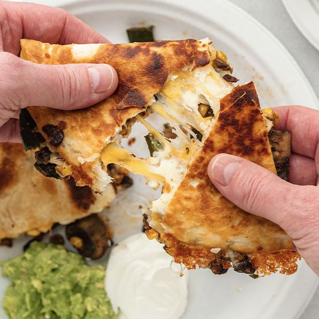 Hands pulling apart a slice of mushroom quesadilla over a Chinet Classic plate