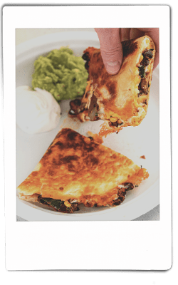 Instax picture of hands pulling apart a slice of mushroom quesadilla over a Chinet Classic plate