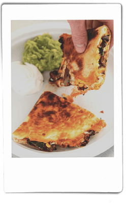 Instax picture of hands pulling apart a slice of mushroom quesadilla over a Chinet Classic plate