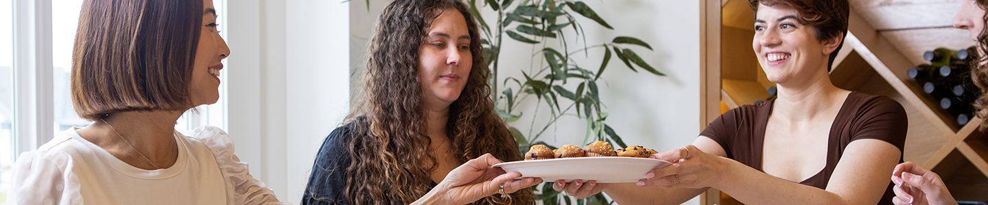 Women passing a Chinet Classic plate with muffins on it