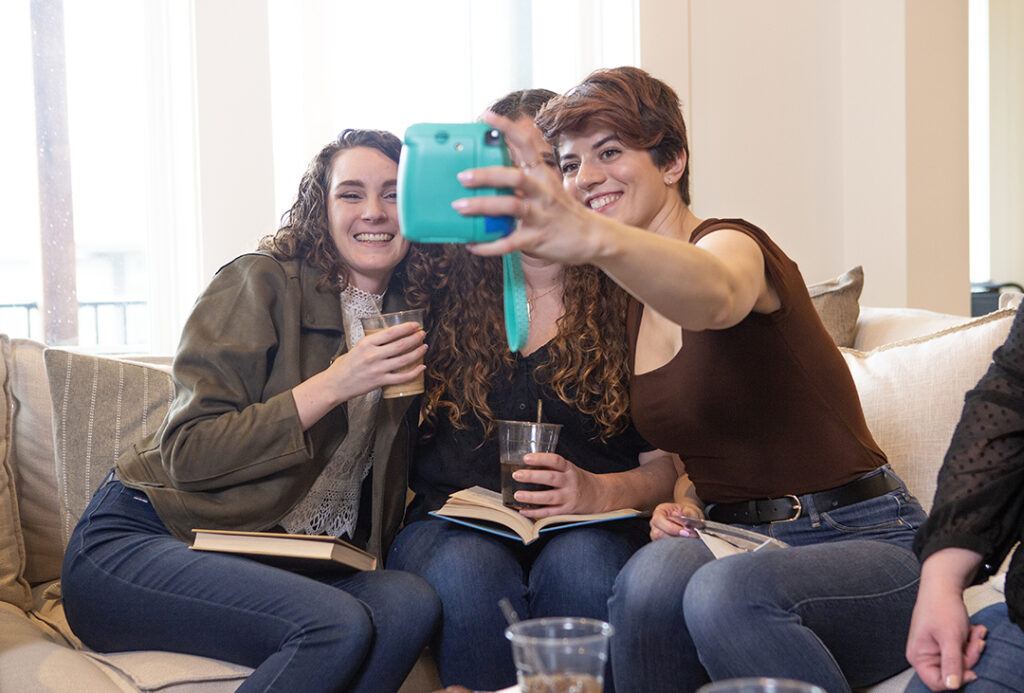 Women sitting on a couch taking an Instax picture of themselves