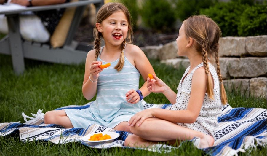 Two girls eating a snack from a Chinet Classic® Lunch plate on a picnic blanket