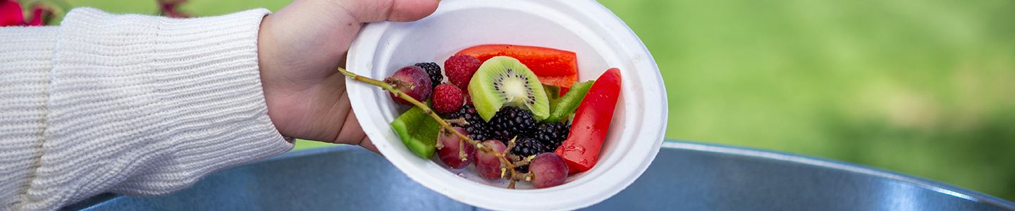 Woman pouring a plate full of leftover food in a compost bin