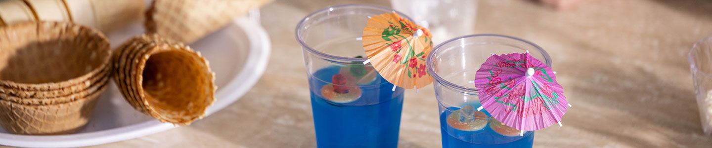 Blue Jell-O in plastic cups sitting on a table with paper drink umbrellas