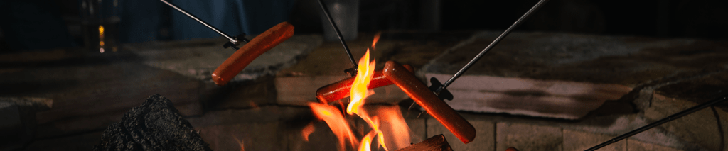 Hotdogs on cooking poles roasting over a bonfire