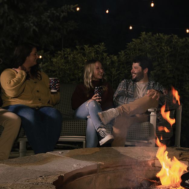 Group of men and women holding Chinet Comfort cups sitting around a bonfire