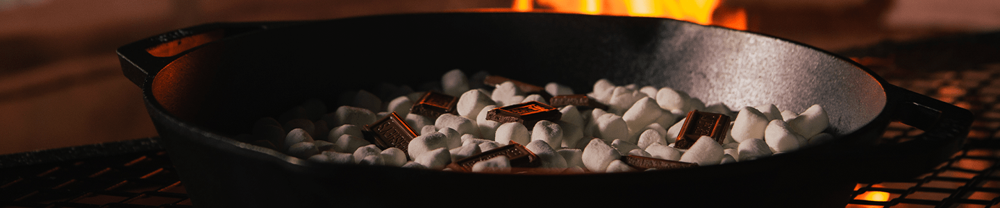 Bonfire smores dip with chocolate and gooey marshmallows cooking over a fire
