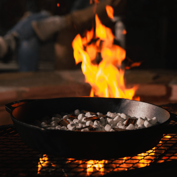 Bonfire smores dip with chocolate and gooey marshmallows cooking over a fire