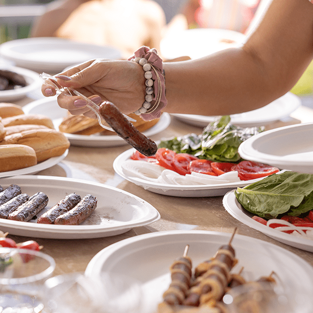 Women's hand picking up a hotdog off a Chinet Classic plate with a fork