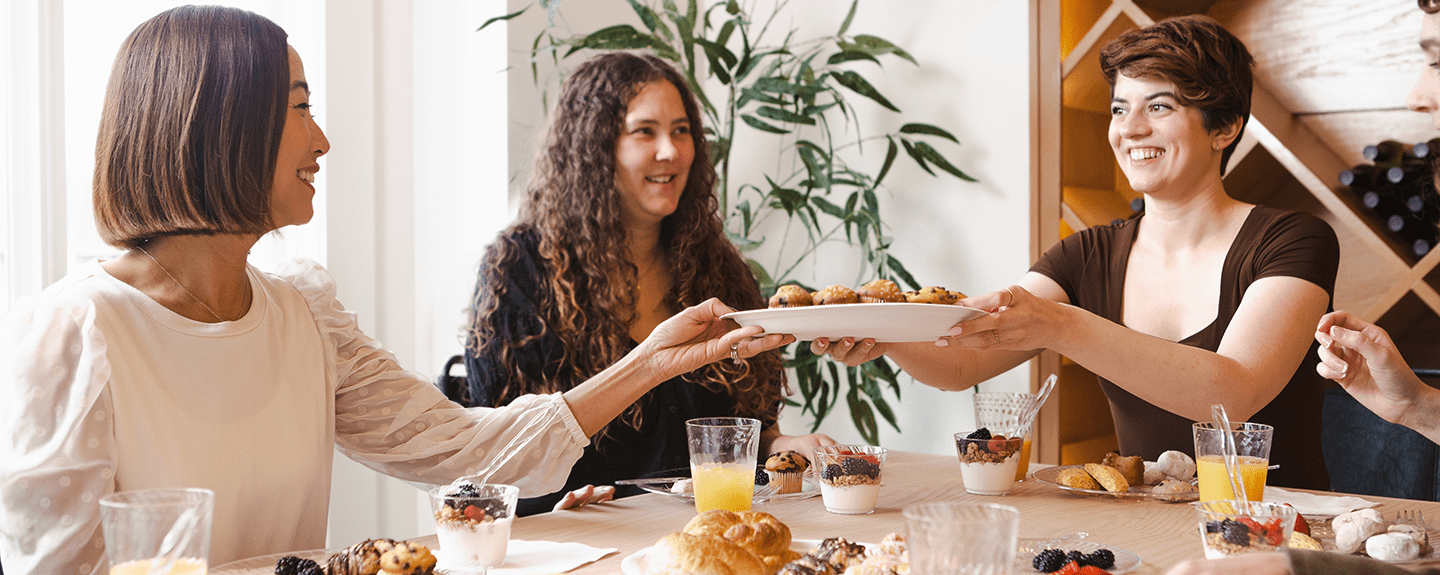 Women passing a Chinet Classic plate of mini muffins across a table