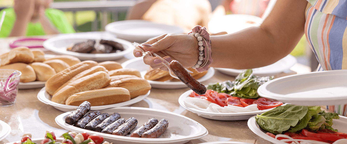 Women's hand picking up a hotdog off a Chinet Classic plate with a fork