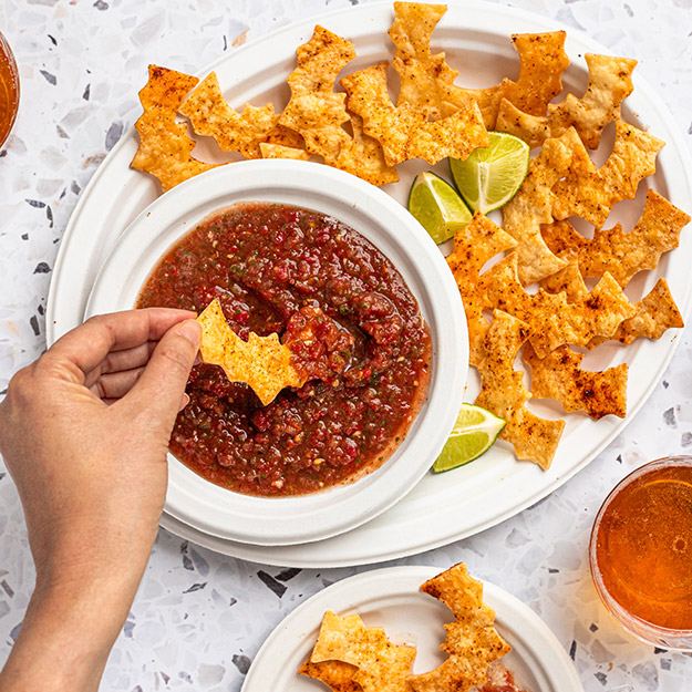 A hand dipping a bat-shaped chip in salsa served in Chinet Classic products