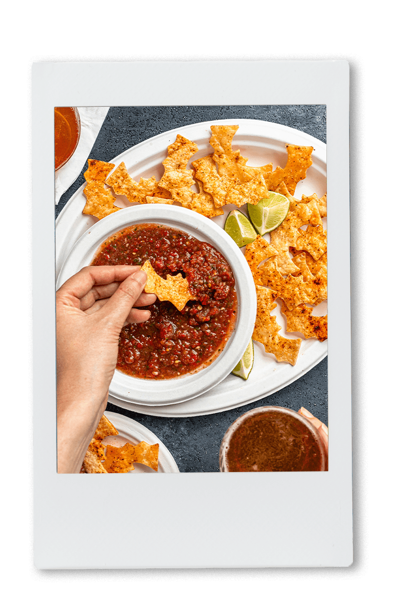 A hand dipping a bat-shaped chip in salsa served in Chinet Classic products