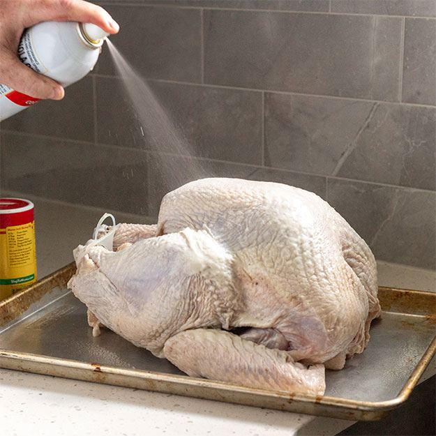 Hand spraying cooking spray on a raw turkey