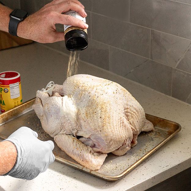Hands sprinkling spices on a raw turkey