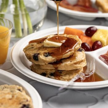 Syrup being poured over Blueberry Lemon Pancakes served on a Chinet compartment plate