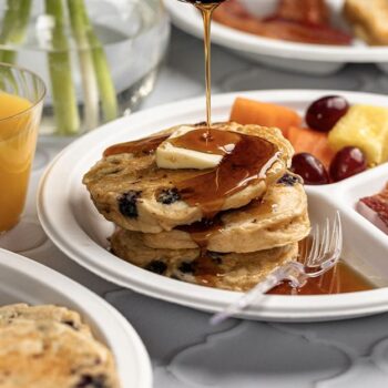 Syrup being poured over Blueberry Lemon Pancakes served on a Chinet compartment plate