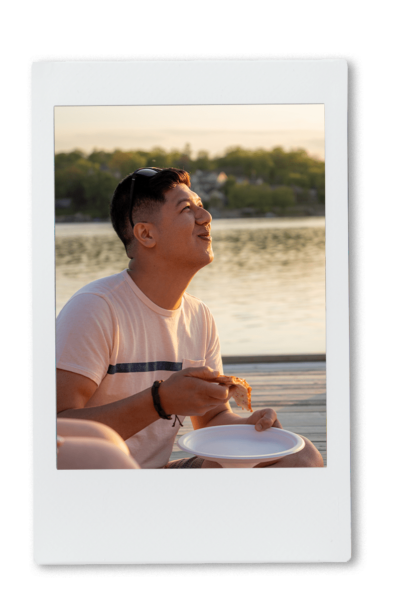 guy laughing and eating pizza on a chinet plate at the lake