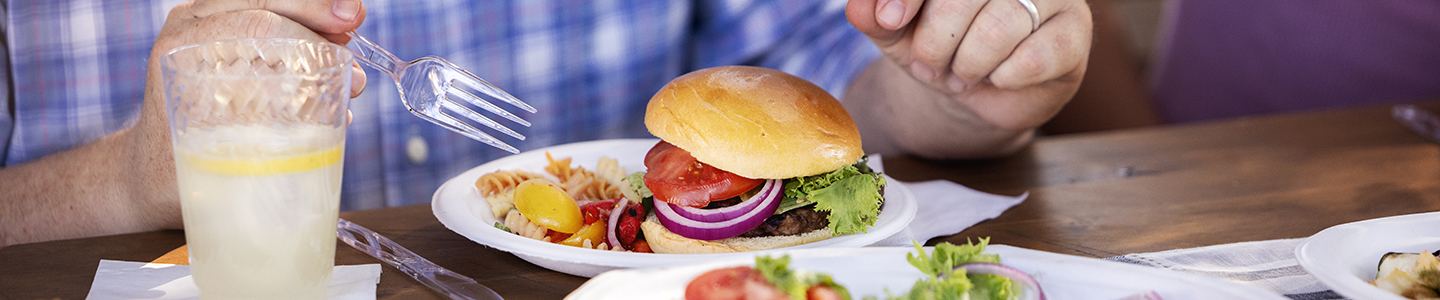 Man cutting into a cheeseburger served on a Chinet Classic plate