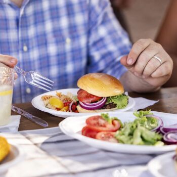 Man cutting into a cheeseburger served on a Chinet Classic plate