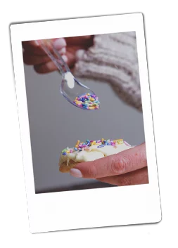 Instax picture of a hand pouring sprinkles on iced cookies