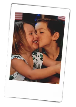 Instax picture of a young brother giving his sister a kiss on her cheek