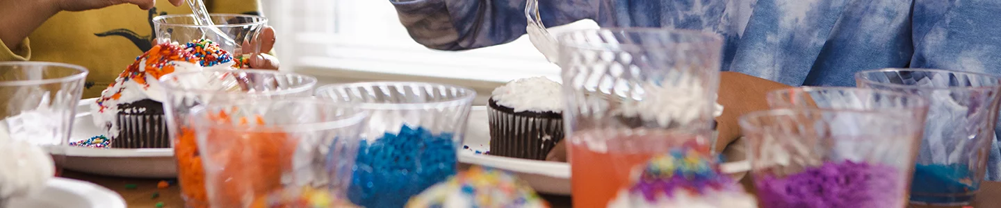 Hands pouring sprinkles on cupcakes