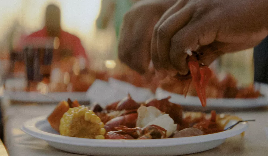 Close up of two hands pulling apart a crawfish above a Chinet Classic® dinner plate full of crawfish and corn
