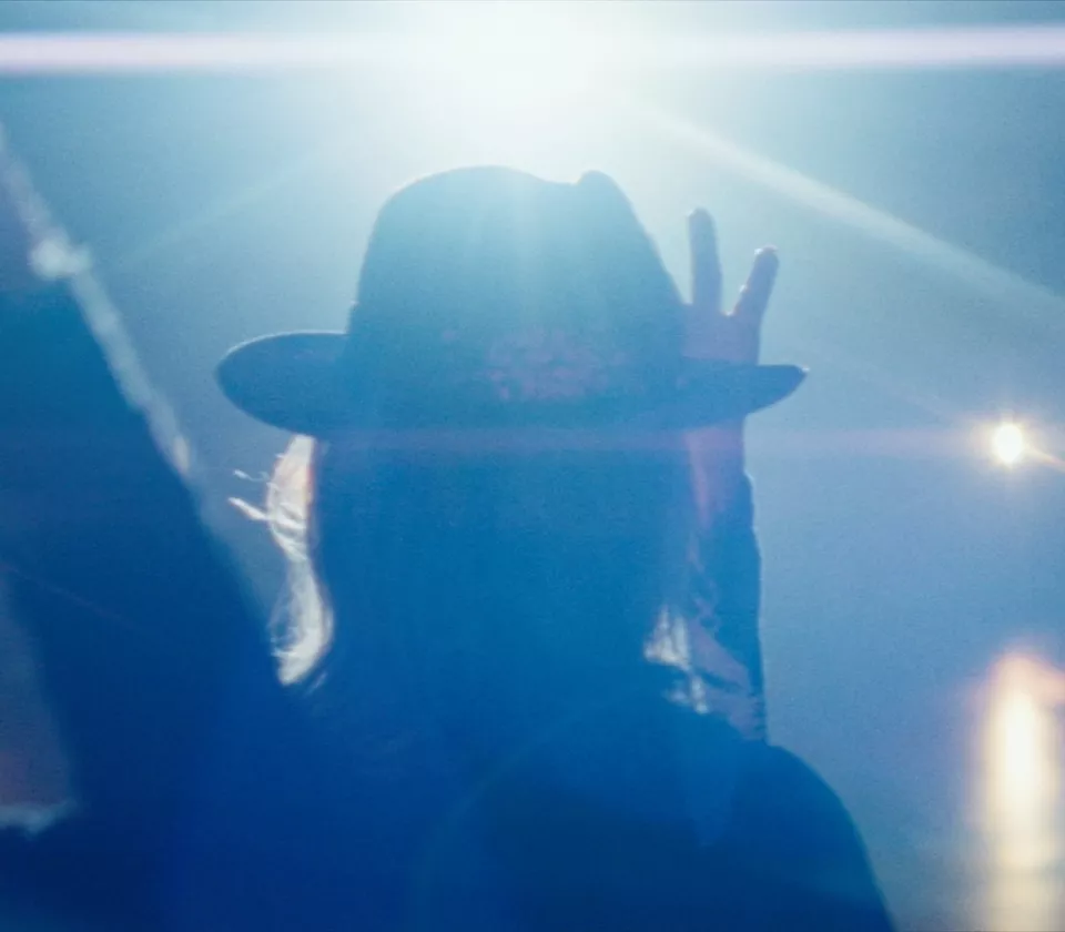 Close up of woman holding brim of hat while stage spotlight shines behind her
