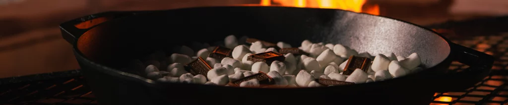 Bonfire smores dip with chocolate and gooey marshmallows cooking over a fire
