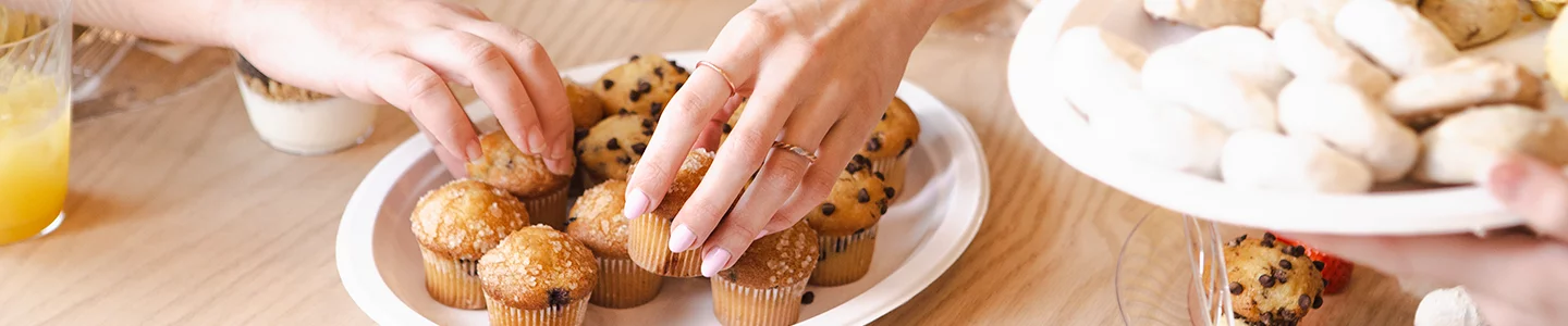 Women's hands grabbing muffins from a Chinet Classic plate