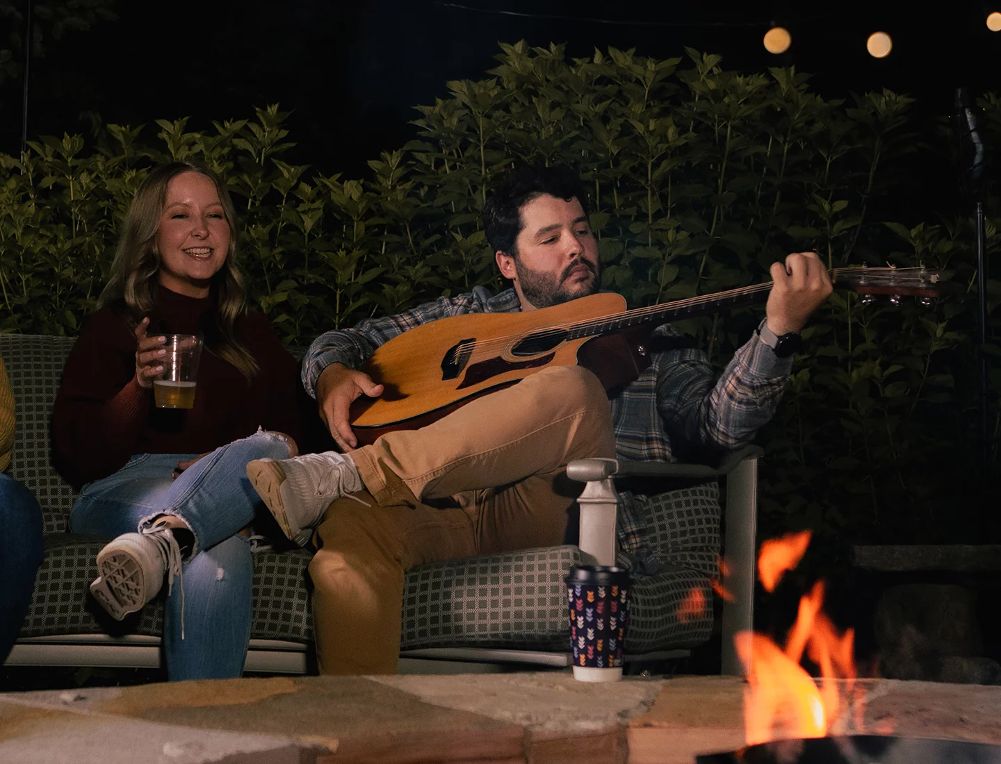 Man holding a guitar sitting with friends around a bonfire